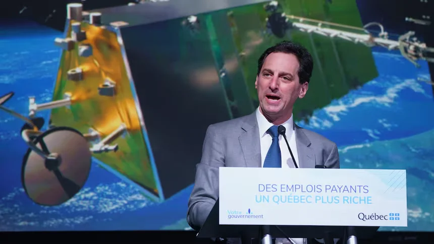 A speaker delivers a speech at a Quebec government event, with an image of a satellite orbiting Earth in the background.